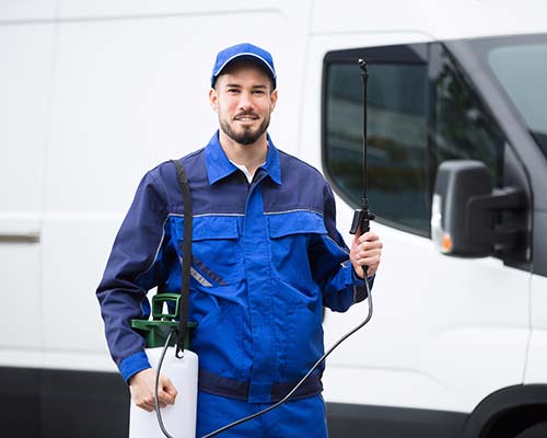 man in a blue exterminator uniform holding a treatment tank